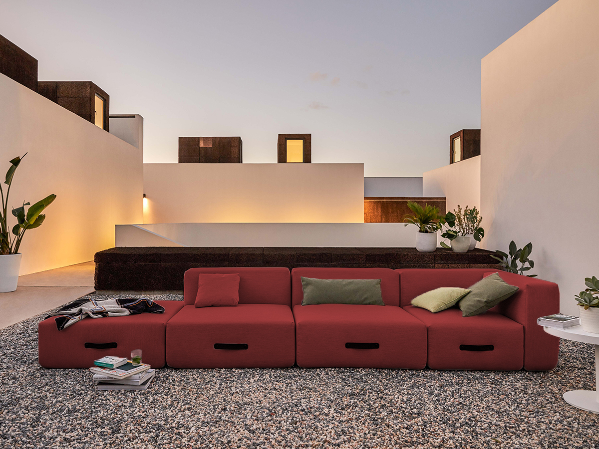Rotes Conmoto Outdoor Sofa mit Kissen auf Kiesboden, moderne Gartenmöbel für Terrasse und Balkon.