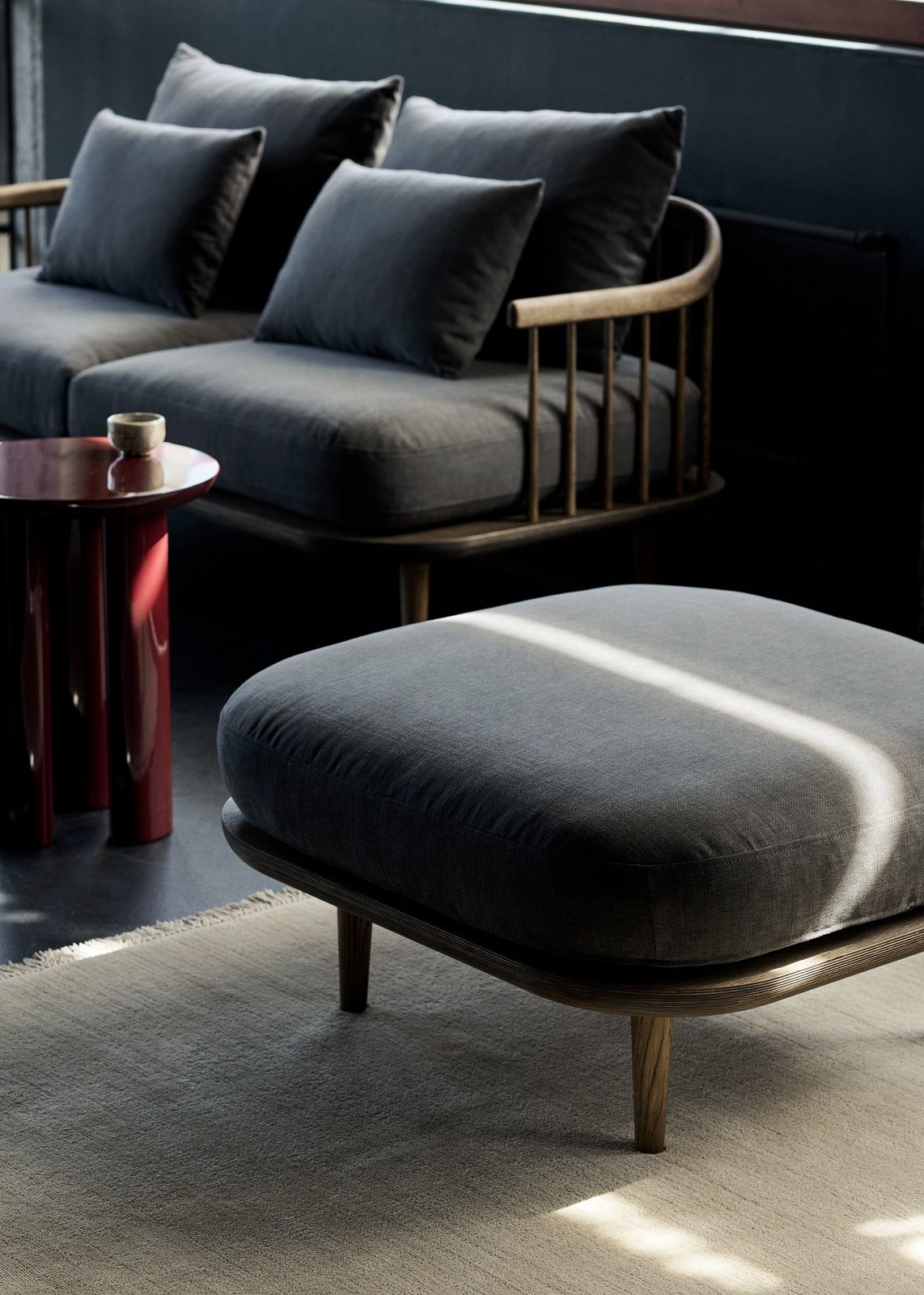 Detailaufnahme des AndTradition The Moor AP19 Teppichs mit grauem Hocker und Sofa im Hintergrund.