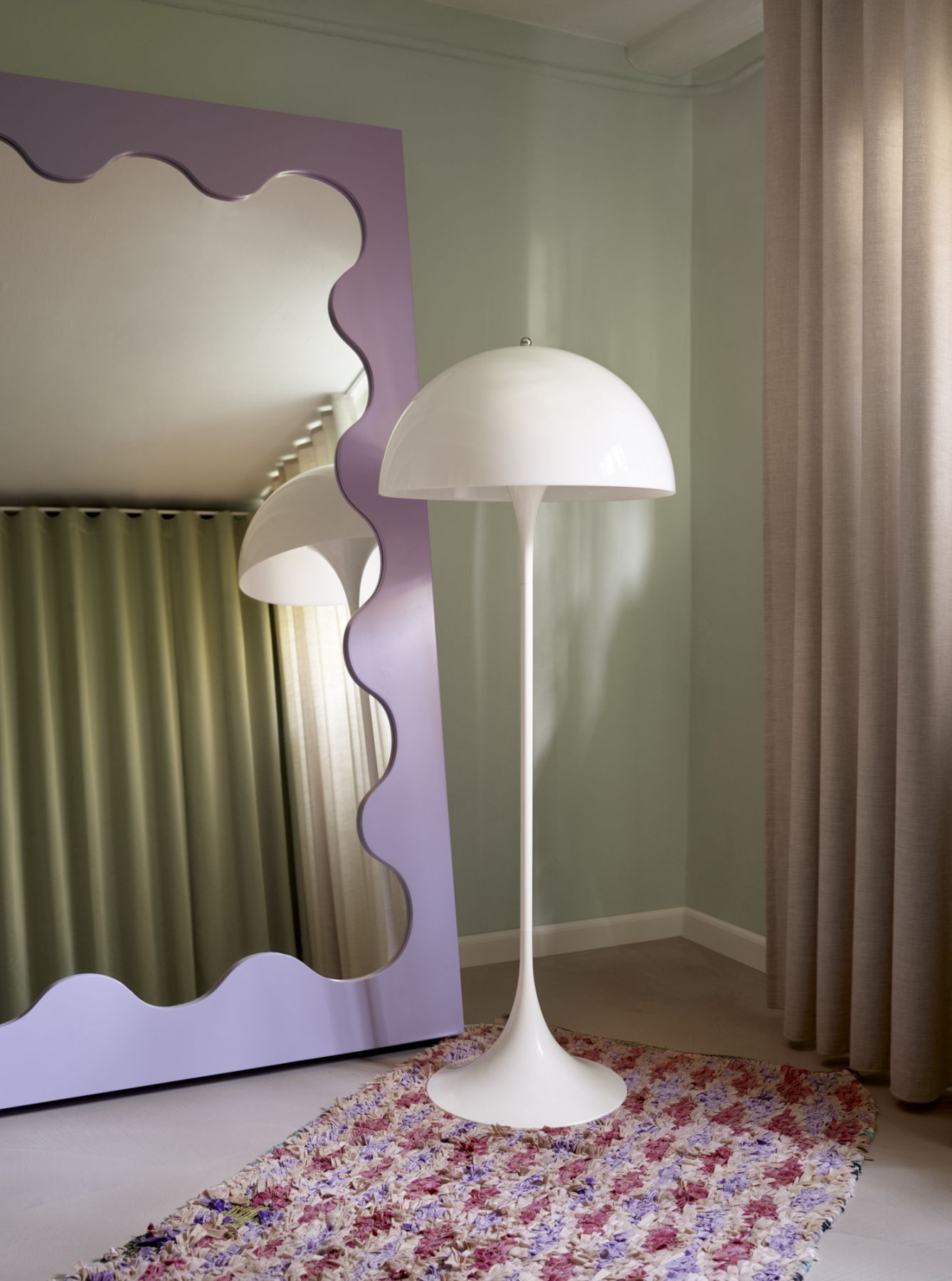 Weiße Stehlampe im Retro-Design neben lila Spiegel mit gewelltem Rahmen auf buntem Teppich.