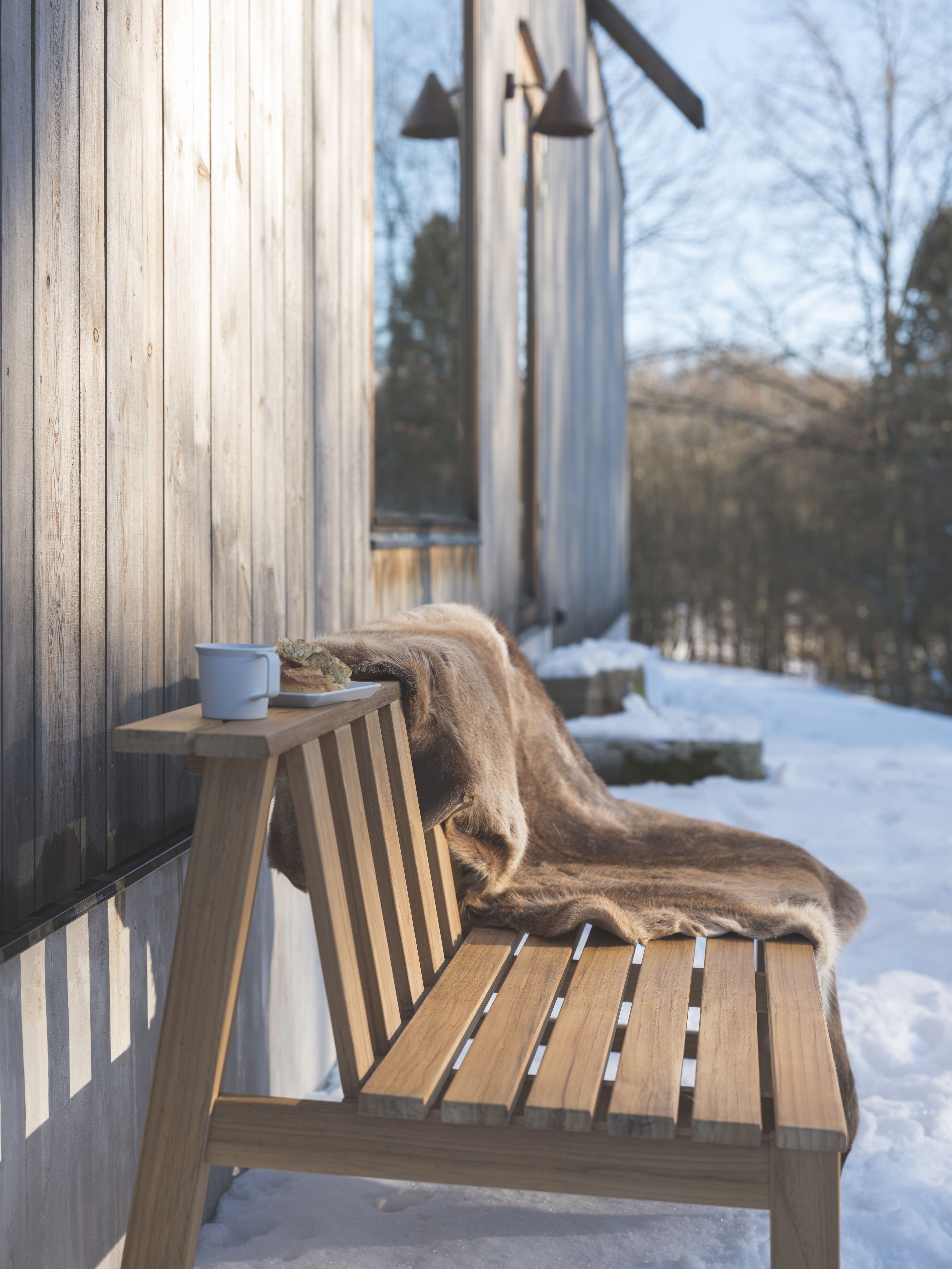 Cadence Bank Teakholz Gartenbank von Fritz Hansen mit Fell, Tasse und Gebäck im Winter.