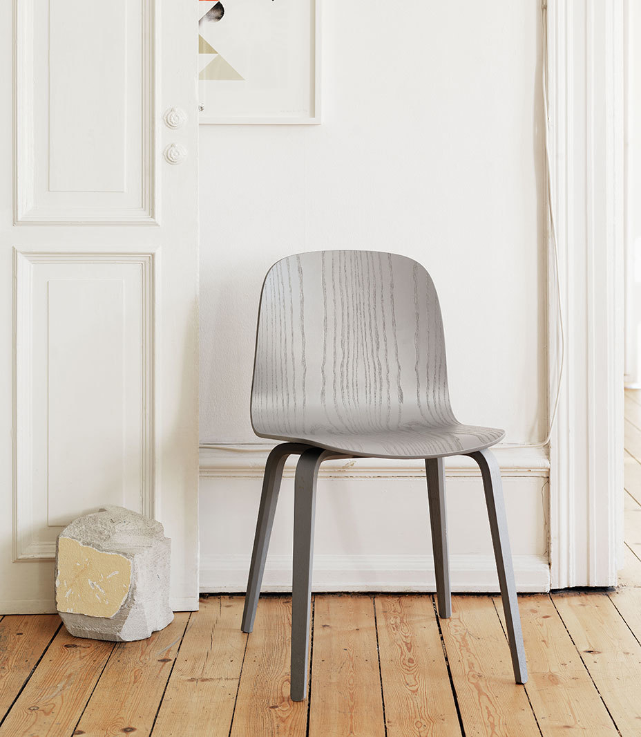 Grauer Visu Chair von Muuto mit Holzbeinen vor weißer Wand und Holzboden. Designstuhl.
