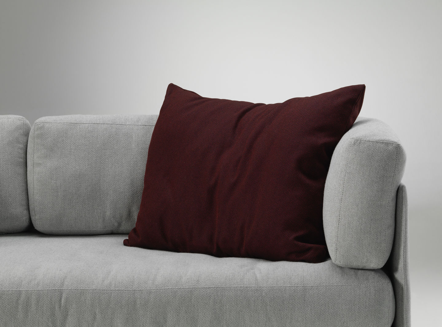 Vitra Kissen in Bordeauxrot auf einem grauen Sofa, modernes Wohnaccessoire für stilvolles Interieur.
