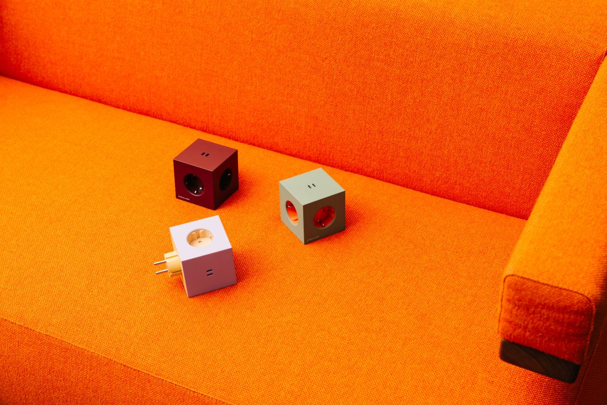 Drei Avolt Square 2 Steckdosenwürfel in Rot, Grün und Weiß auf einem orangefarbenen Sofa.