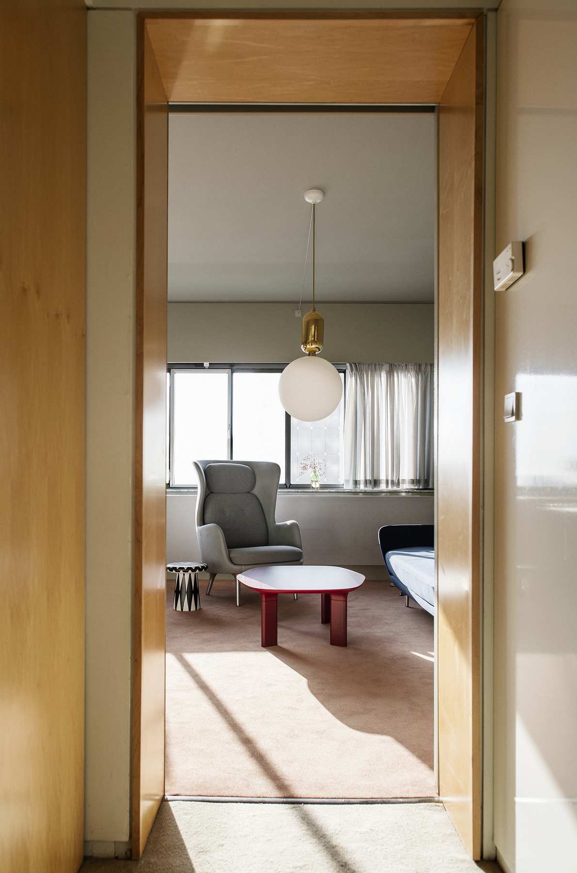 Wohnzimmer mit Fritz Hansen Analog Tisch in Rot, Sessel, Lampe und Fenster mit Vorhängen.