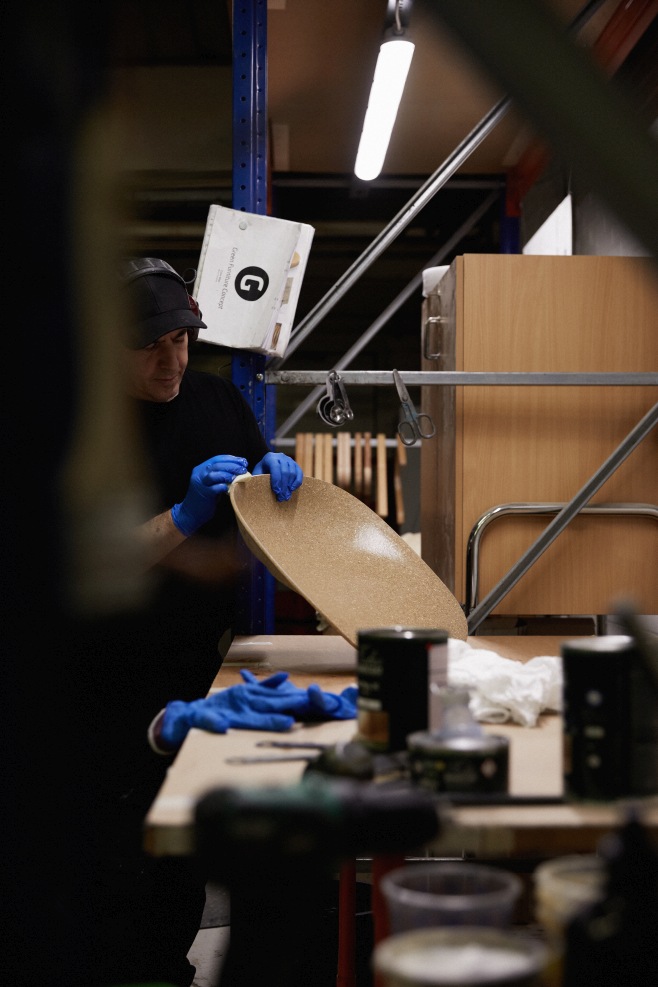 Handwerker bearbeitet Sitzfläche eines Normann Copenhagen Mat Chair Holz Stuhls in Werkstatt, Fokus auf nachhaltige Möbelproduktion.