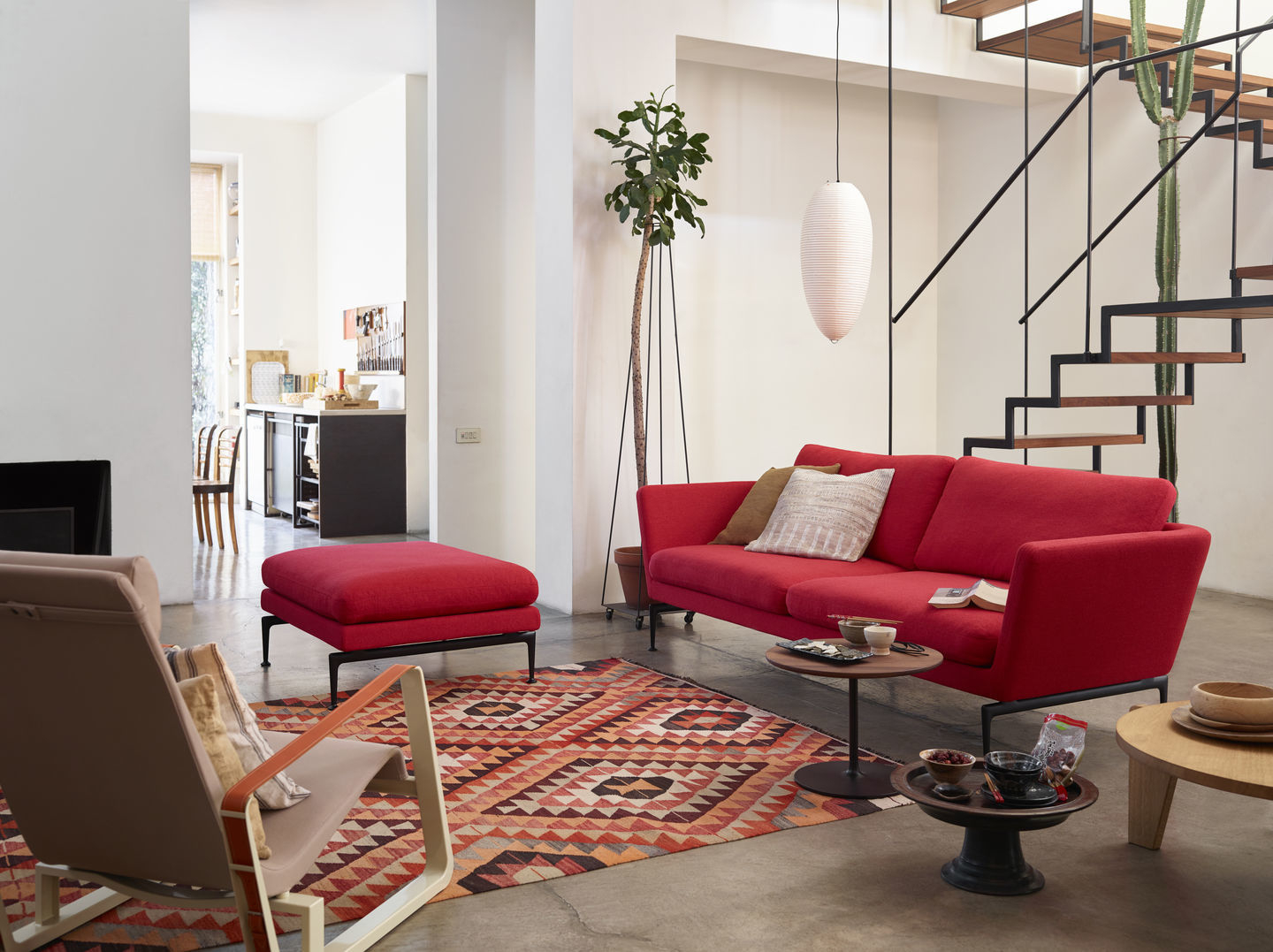 Wohnzimmer mit rotem Vitra Cité Sessel, passendem Hocker und Teppich mit geometrischen Mustern.
