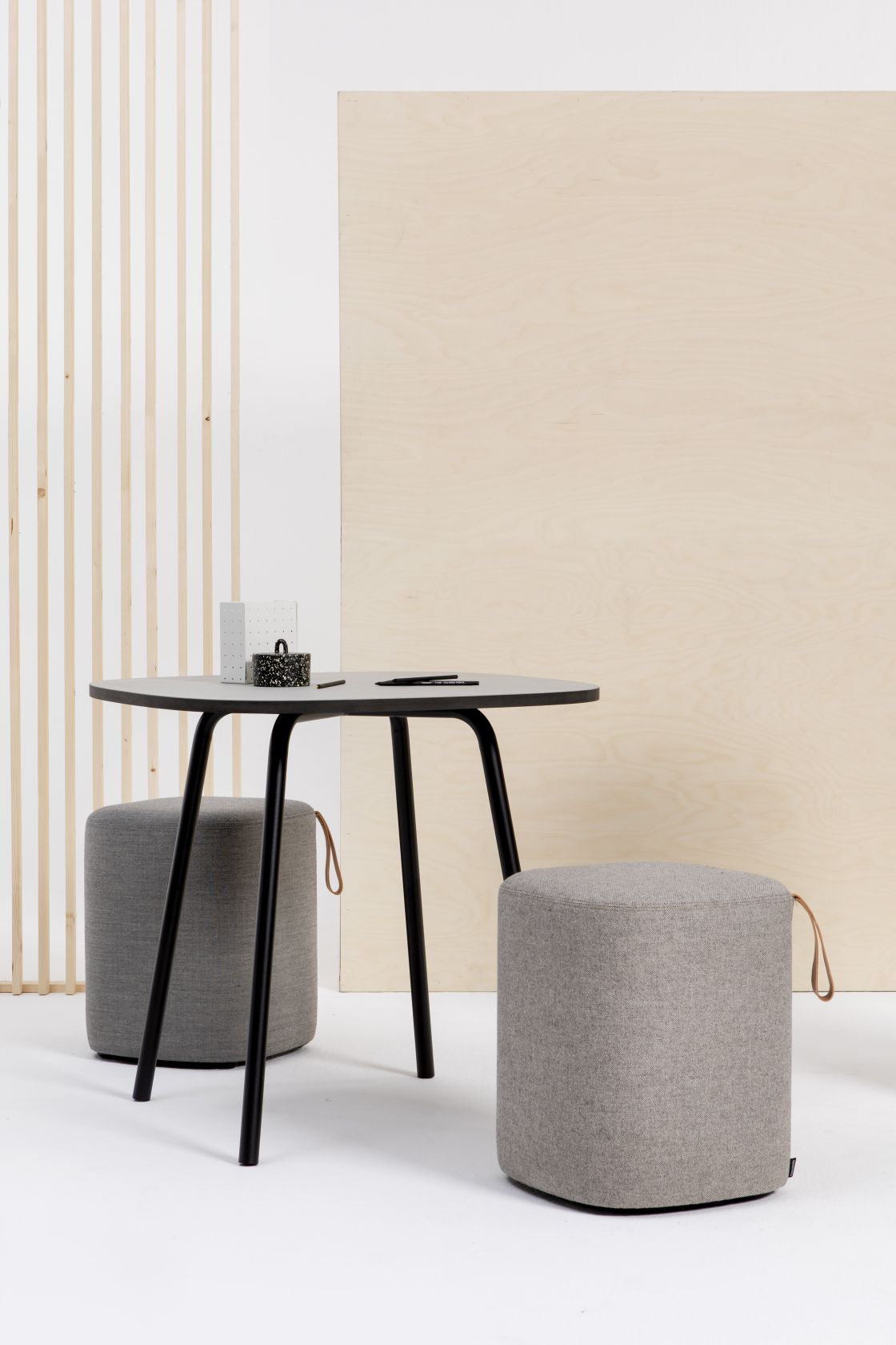 Grauer Pully Hocker von Cascando neben einem Tisch, ideal als Sitzgelegenheit für Büro und Wartebereich.
