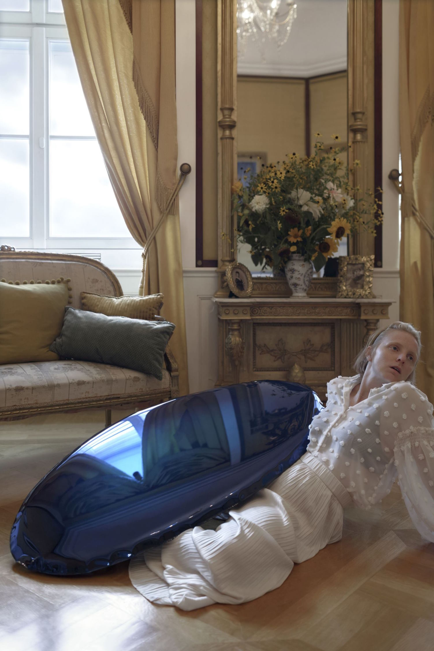 Frau in weißer Bluse und Rock mit blauem, glänzendem Objekt in luxuriösem Interieur.