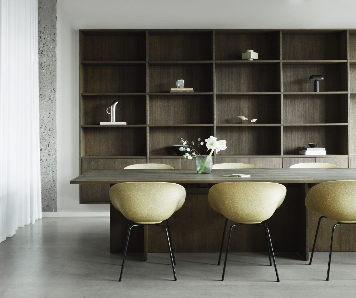 Gelbe Mat Armchair Stühle von Normann Copenhagen am Esstisch vor dunklem Holzregal.