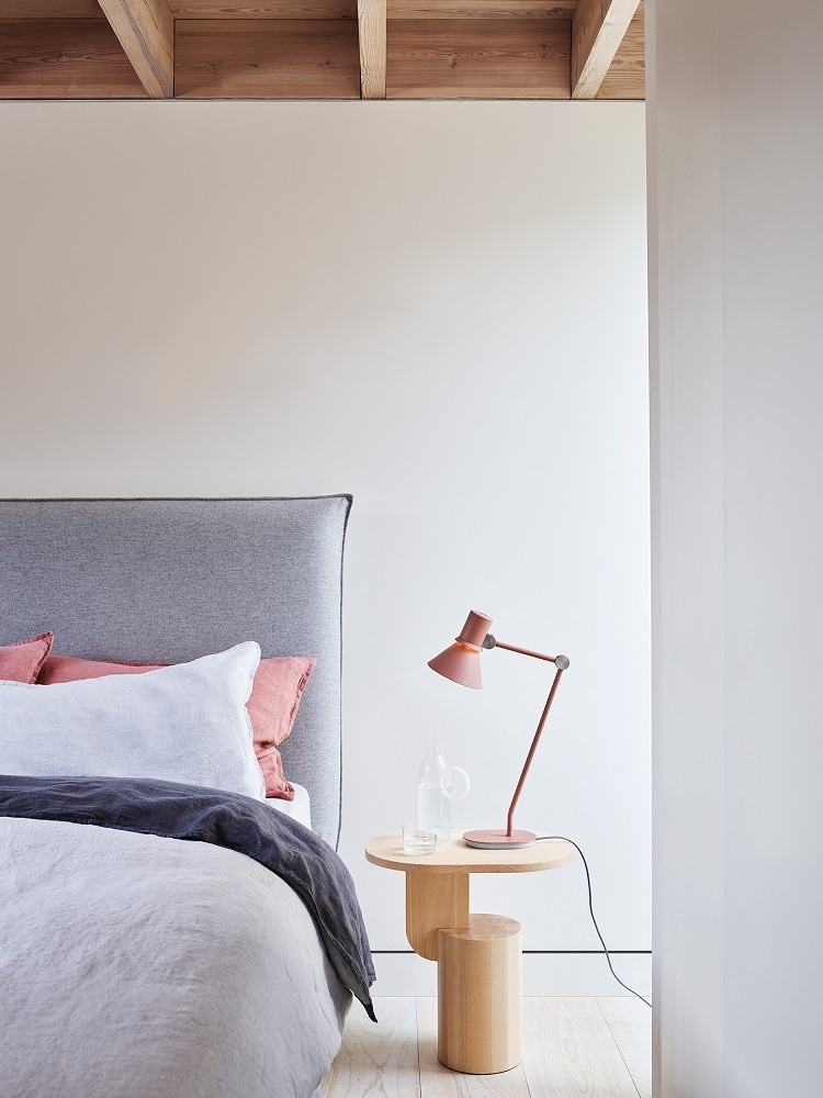 Rosa Anglepoise Type 80 Tischleuchte auf Nachttisch neben Bett mit grauer Bettwäsche und Holzbalkendecke.