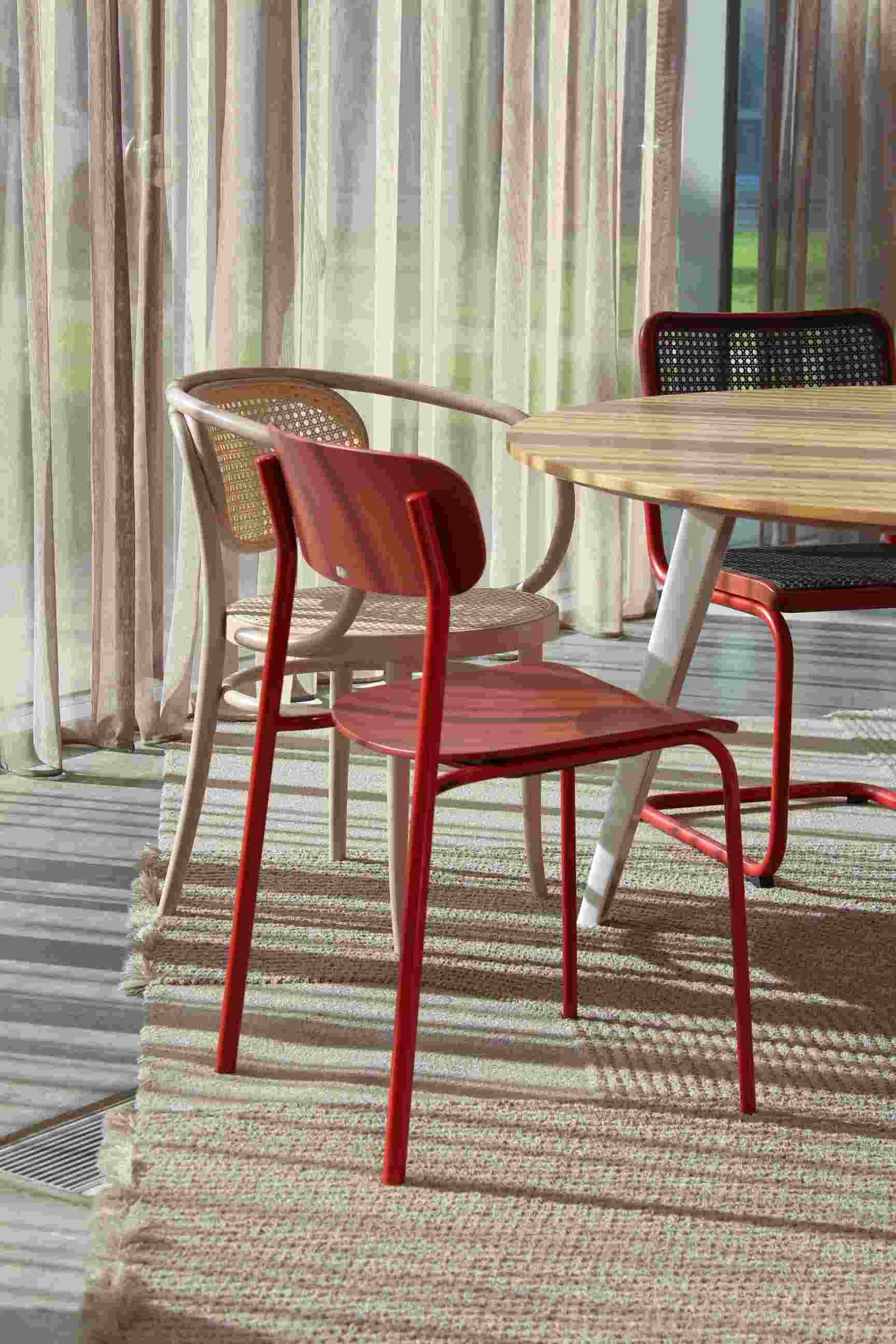 Thonet S 243 Stahlrohrstuhl in Olivgrün, roter Stahlrohrstuhl und Rattanstuhl am Esstisch, modernes Möbeldesign.