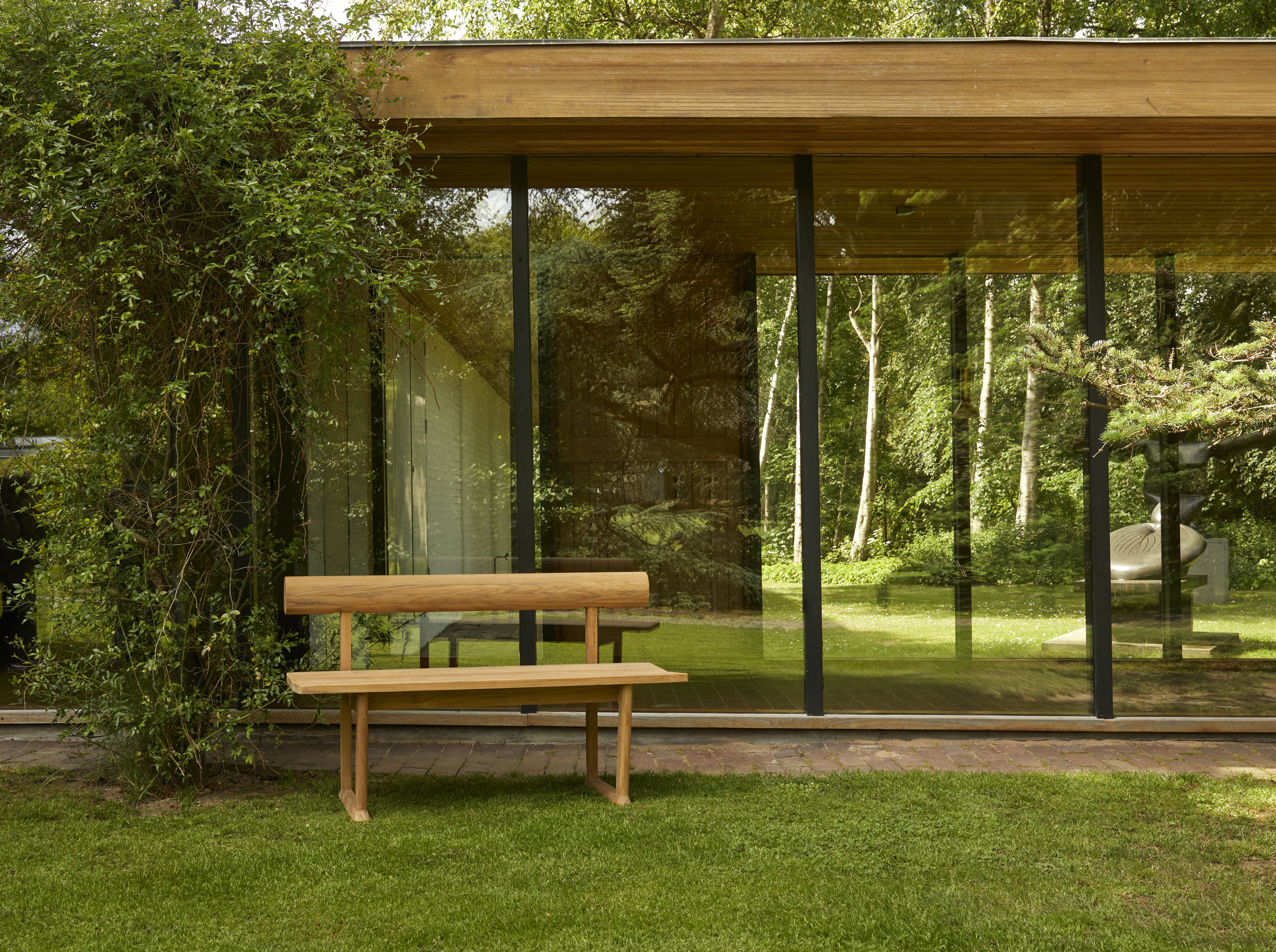 Banco Bank Teak Outdoor von Skagerak by Fritz Hansen auf Rasen vor modernem Haus mit Glasfassade.