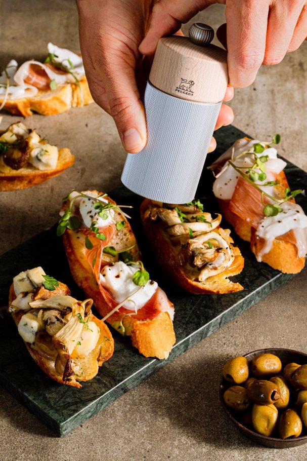 Peugeot Line Salzmühle aus Aluminium und Holz, 12 cm, wird über Bruschetta gehalten.