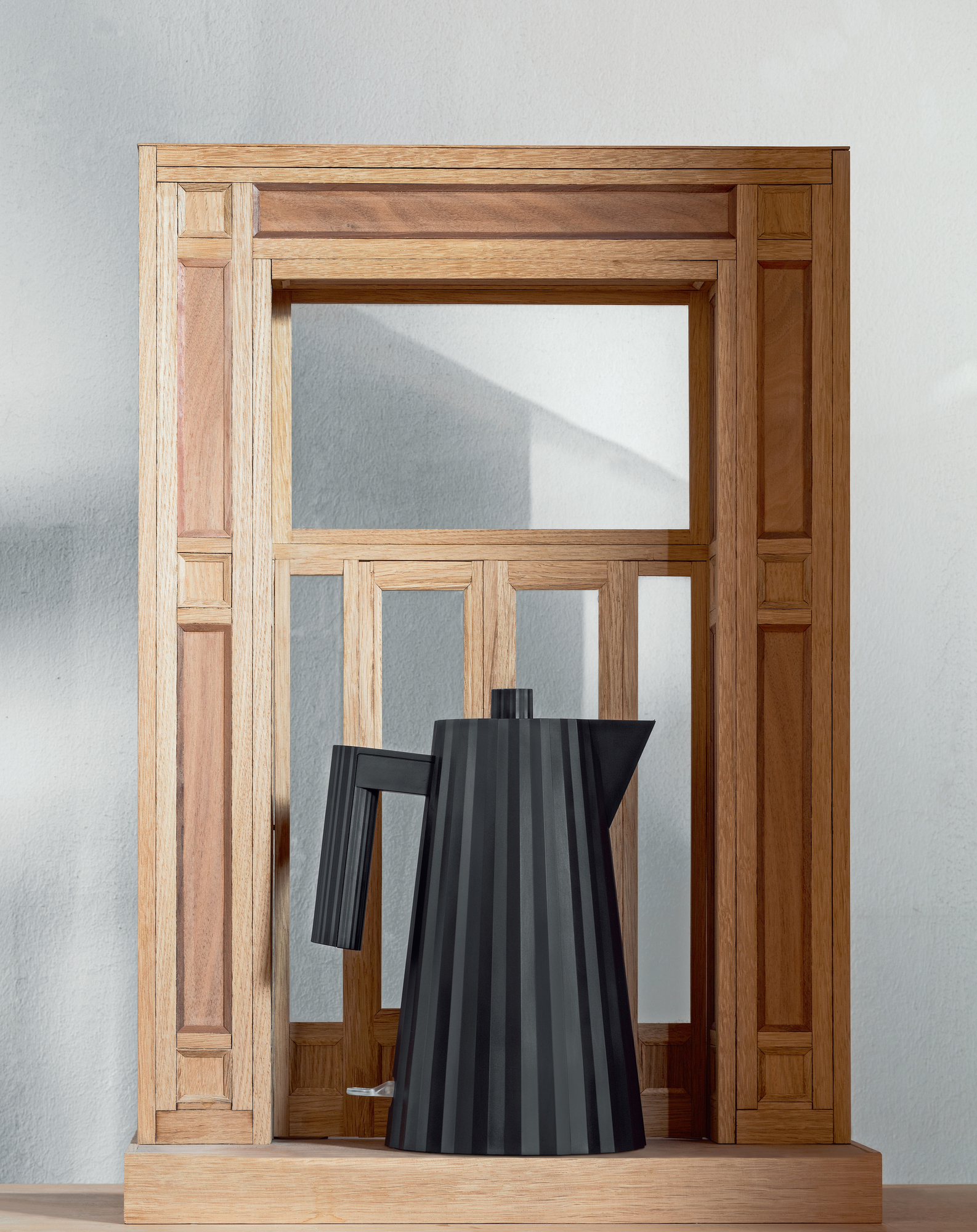 Weißer Alessi Plissé Wasserkocher Small MDL06/W vor einem Holzrahmen, modernes Küchendesign.