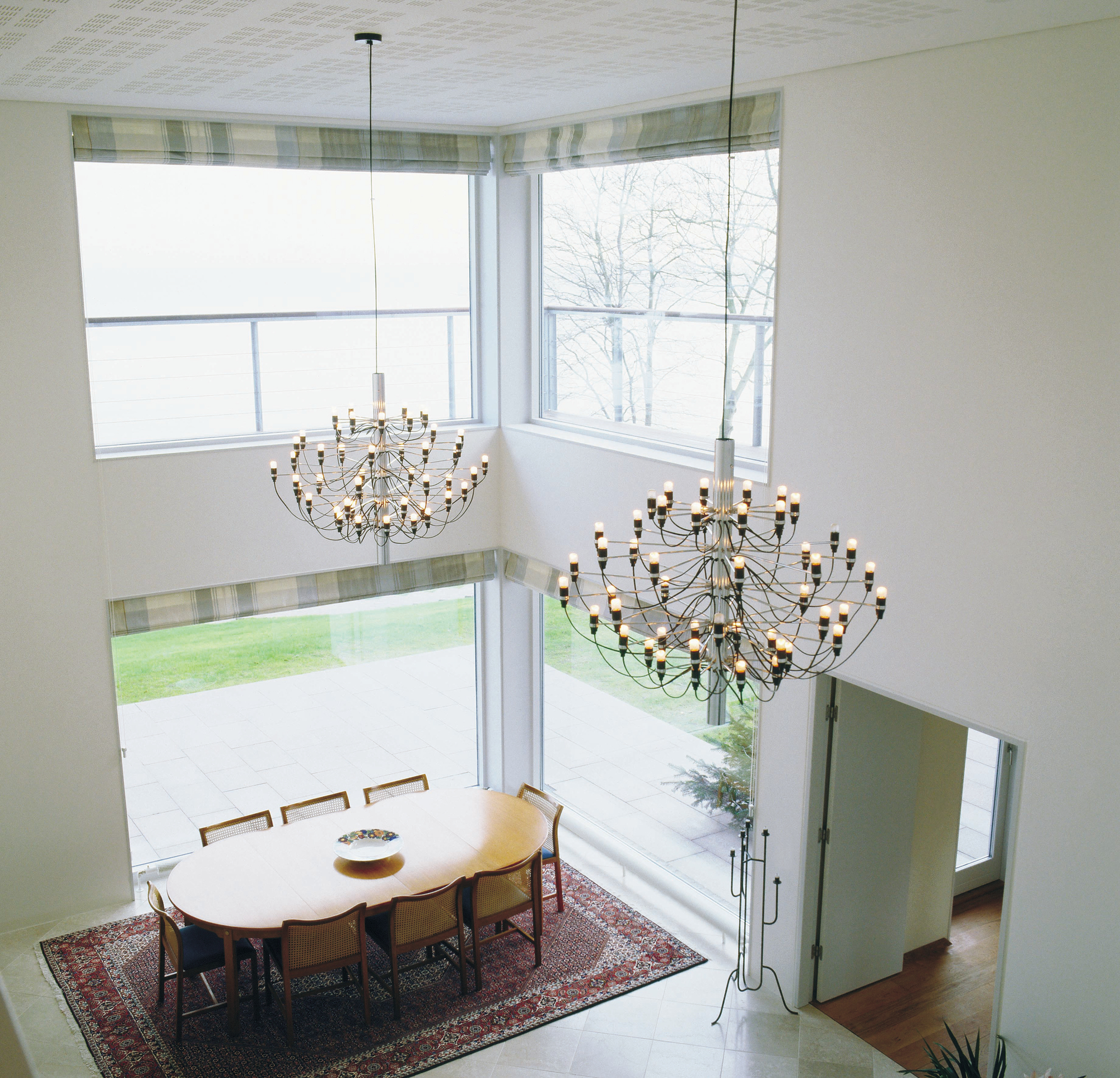Helle, moderne Wohnung mit zwei Flos 2097 Kronleuchtern und mattierten Glühbirnen über einem Esstisch.