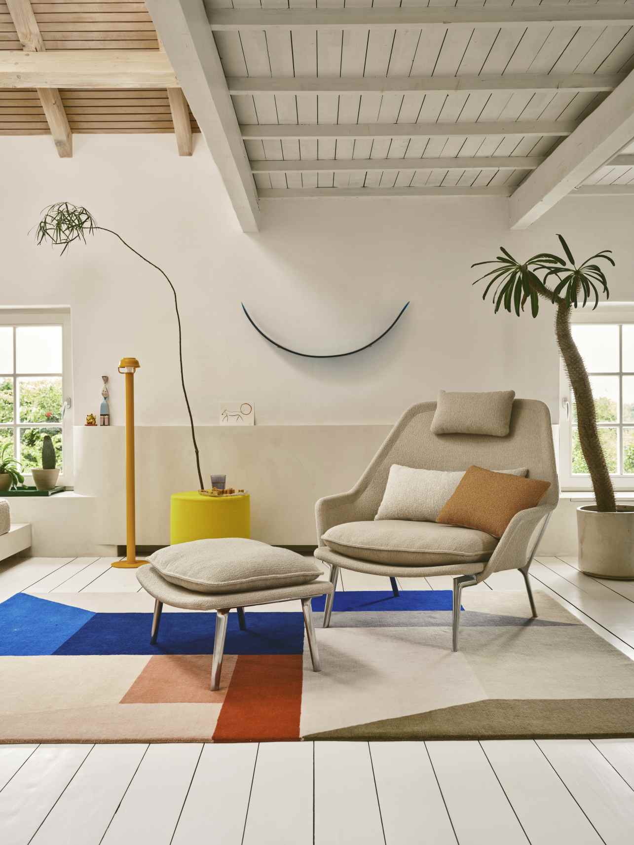 Vitra Slow Chair Sessel mit Hocker in beigem Stoffbezug und Kissen im Wohnzimmer.