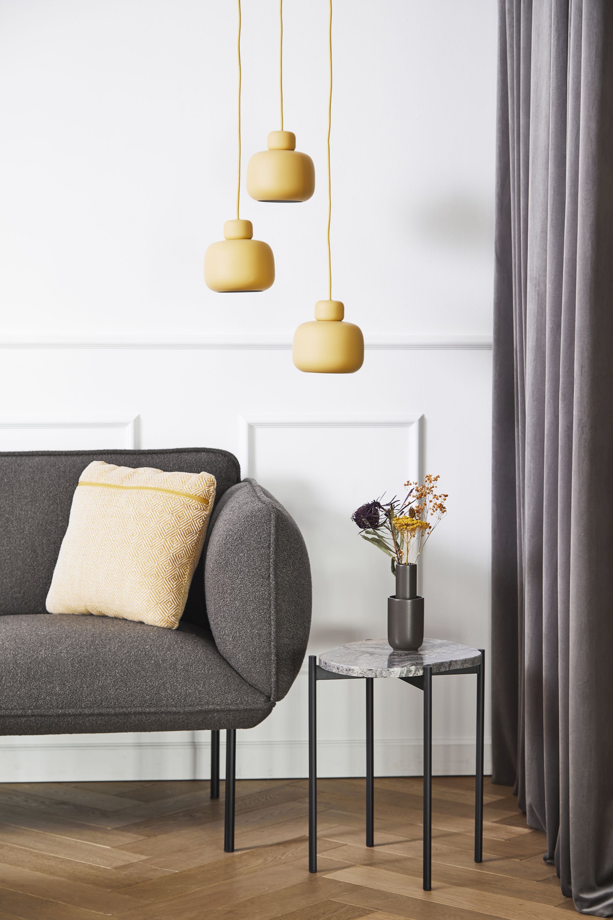 Drei gelbe Stone Pendant Pendelleuchten von Woud über einem grauen Sofa und Beistelltisch.