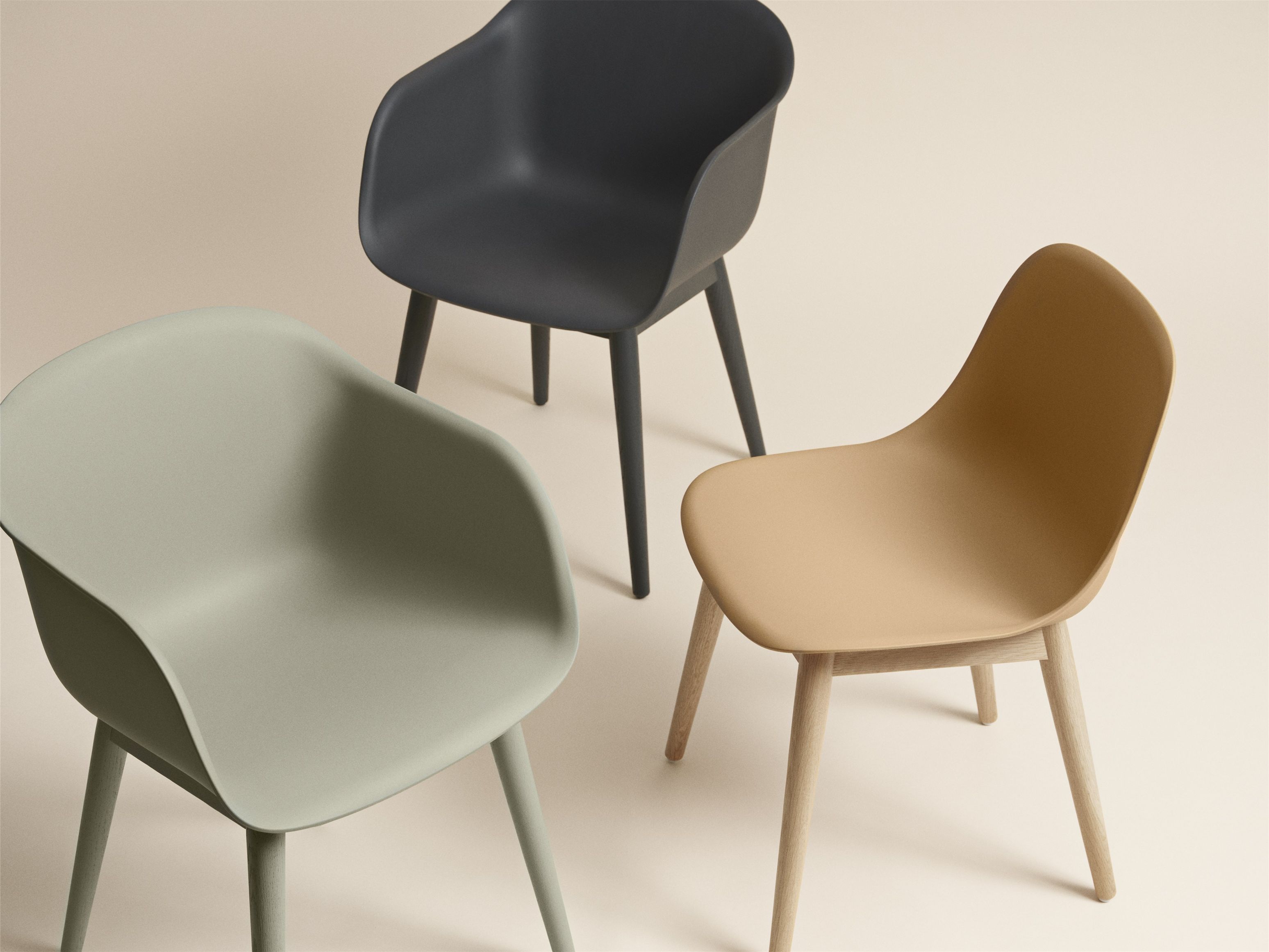Drei Muuto Fiber Armchair Stühle mit Holzgestell in Schwarz, Beige und Grün auf beigem Hintergrund.