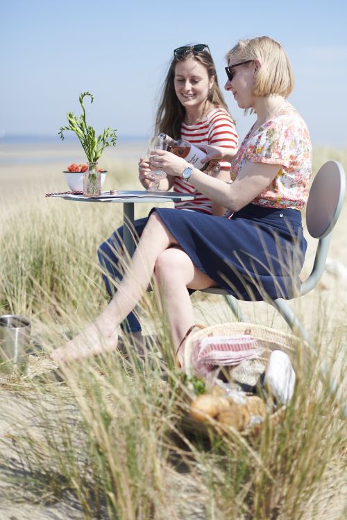 Zwei Frauen sitzen am Strand an einem Bistroo Tisch und genießen ein Getränk.