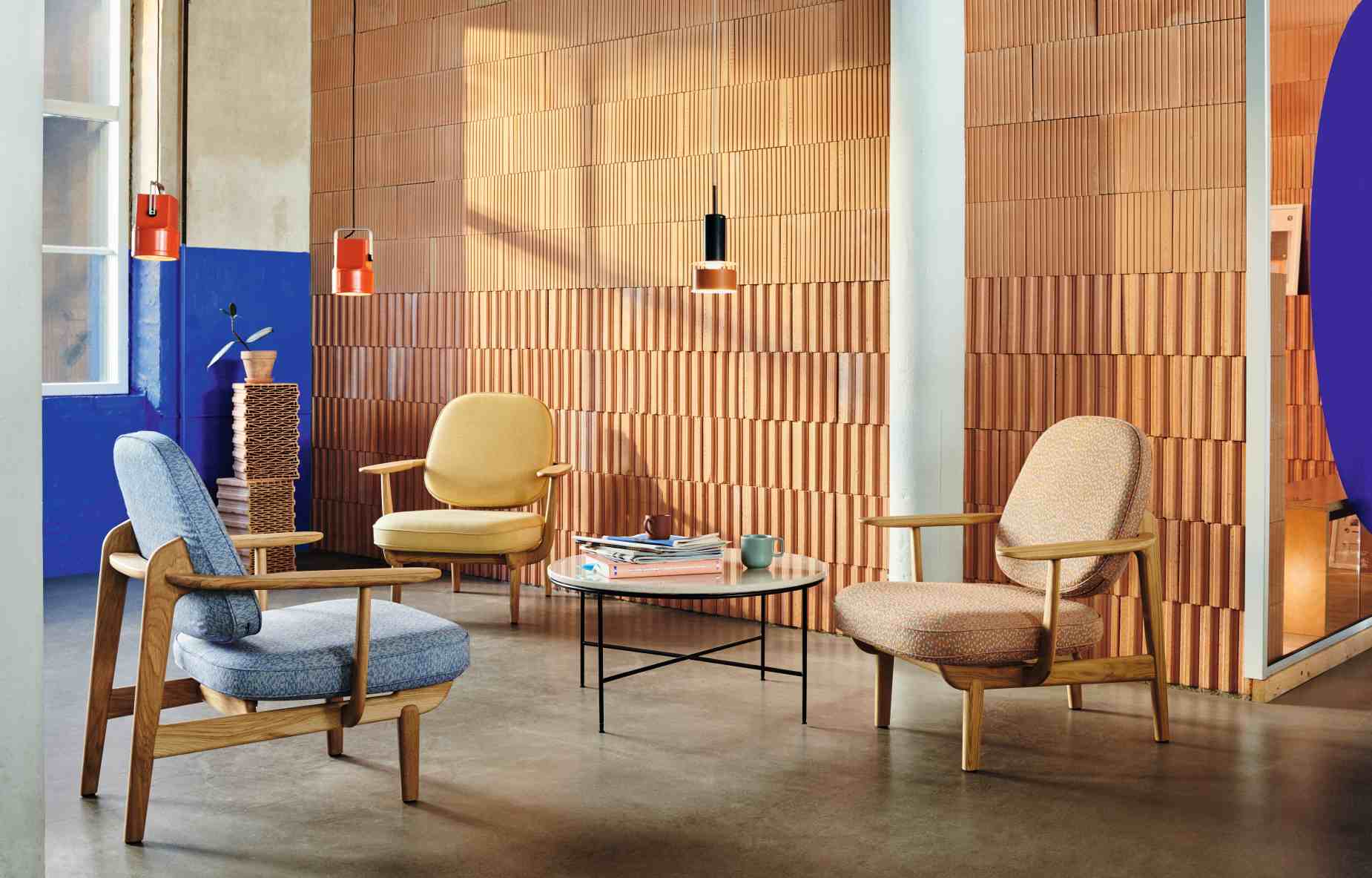 Interieur mit drei Fritz Hansen Fred Loungesesseln in Gelb, Blau und Beige um einen Tisch.