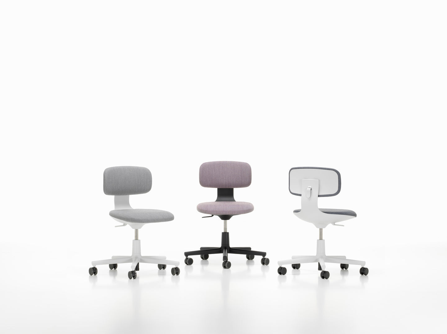 Drei Vitra Rookie Bürodrehstühle in Grau, Lila und Weiß mit Rollen vor einem weißen Hintergrund.
