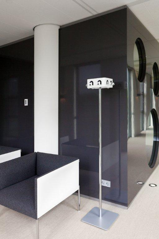 Moderner Wartebereich mit grau-weißem Sessel, Garderobenständer und dunkler Wand mit runden Fenstern für stilvolles Bürodesign.