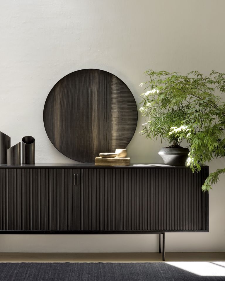 Schwarzes Sideboard mit geriffelter Front, runder Dekoteller, Pflanze und Deko-Objekten für stilvolles Wohnzimmer.
