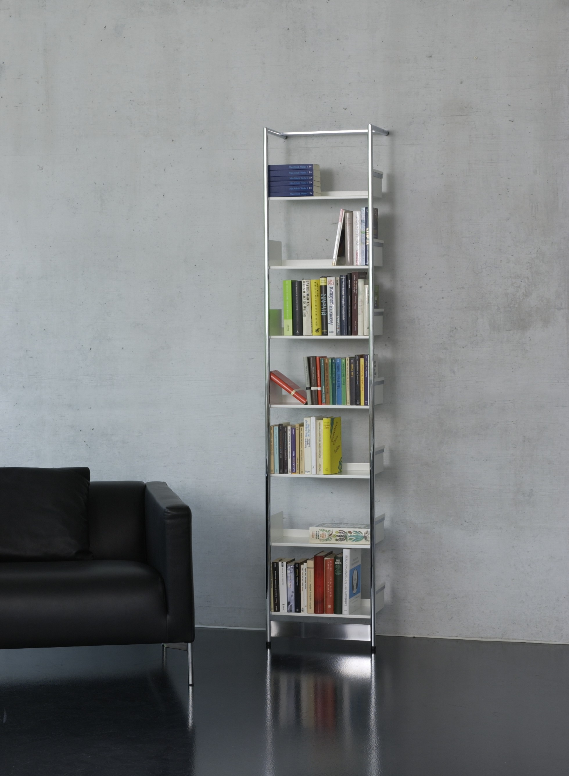 Pool 196 Medium Anlehnregal von Mox, freistehendes Bücherregal aus Stahl und weißen Regalböden, neben schwarzem Sofa.
