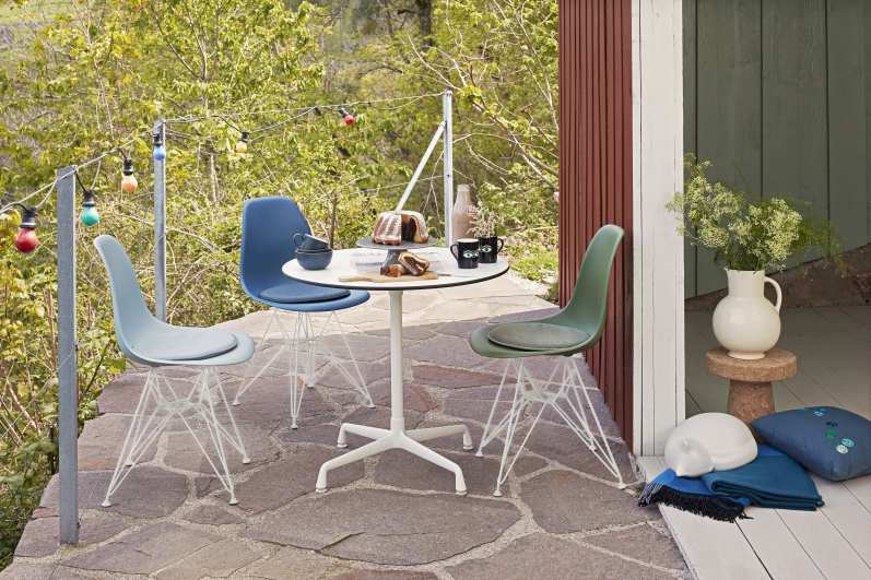 Draußen-Szene mit rundem, weißen Eames Contract Table von Vitra, umgeben von drei farbigen Stühlen.