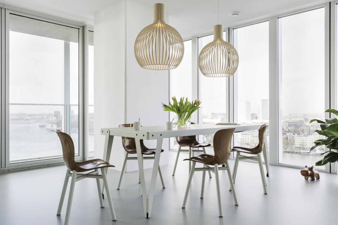 Esszimmer mit Lloyd Indoor Table Tisch, Holzstühlen und modernen Pendelleuchten vor Fensterfront.