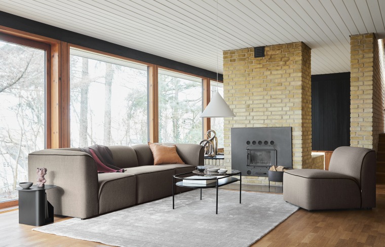 Heller Wohnraum mit großem, hellgrauem Tint Rug Teppich von Woud, Sofa, Sessel und Kamin.