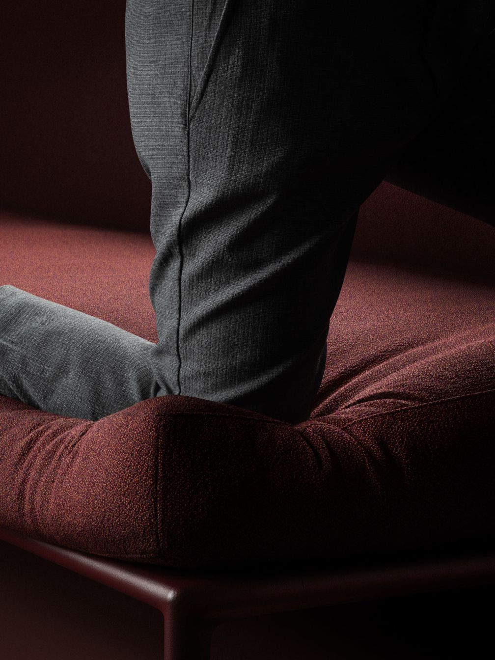 Detailaufnahme: Graue Stoffhose auf einem roten Sofa mit strukturierter Oberfläche.