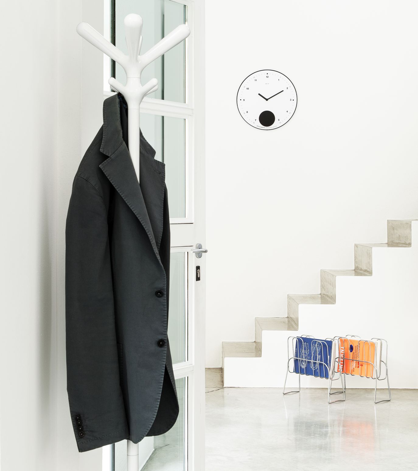 Weißer Pop Kleiderständer von Rexite mit Jacke im minimalistischen Flur mit Treppe und Uhr.