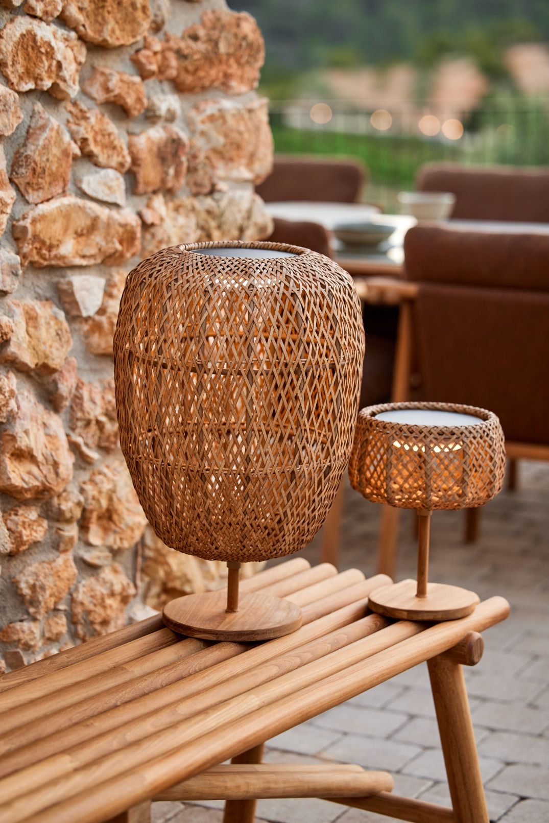 Cane-Line Illusion Glow Tischleuchte: Zwei Outdoor-Lampen aus Rattan auf einer Holzbank.