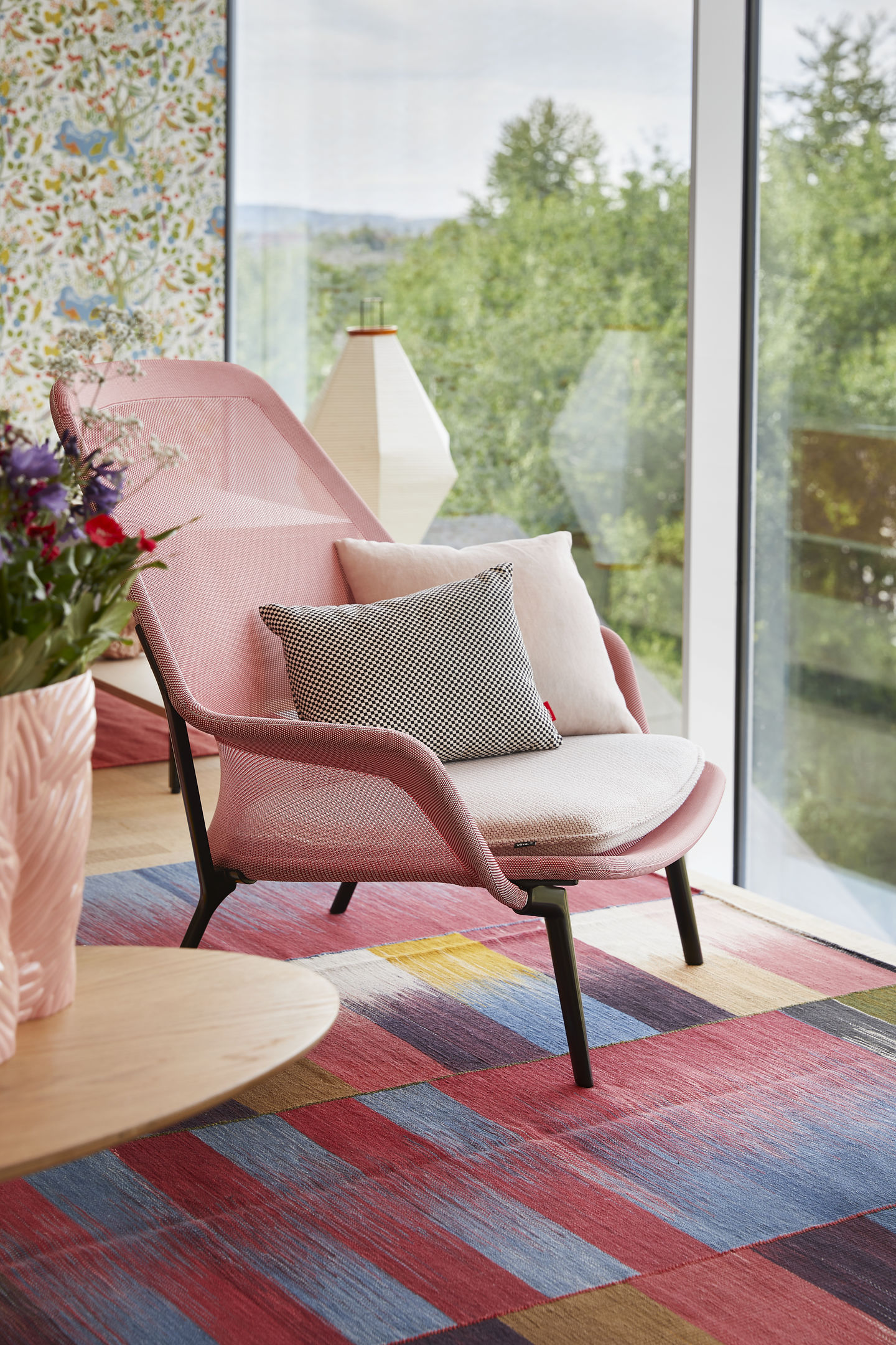 Vitra Slow Chair Sessel in Rosa mit Kissen und Ottoman vor Fenster mit Gartenblick.
