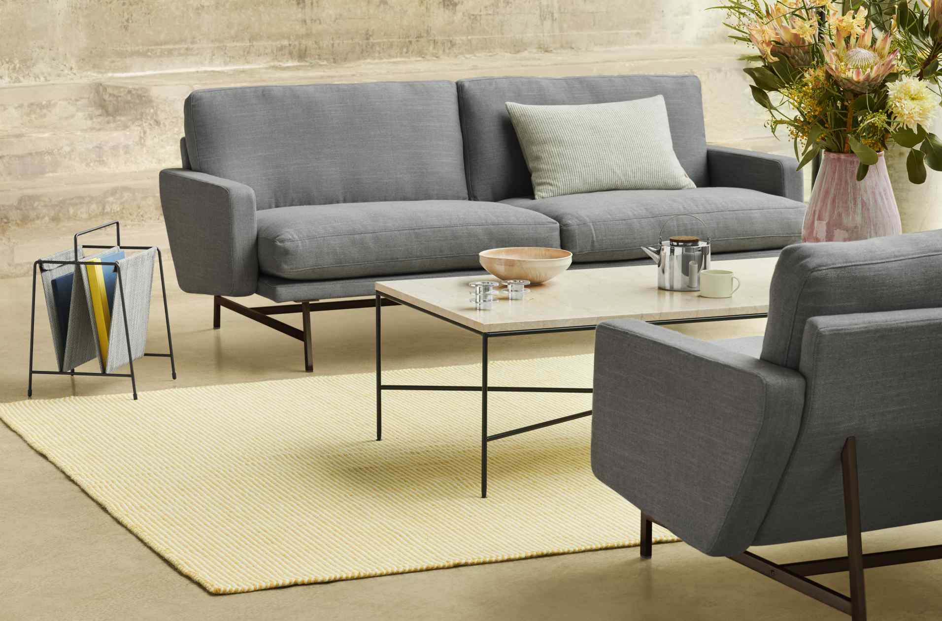 Fritz Hansen Planner Couchtisch aus Marmor mit grauer Couch, Sessel und gelbem Teppich.