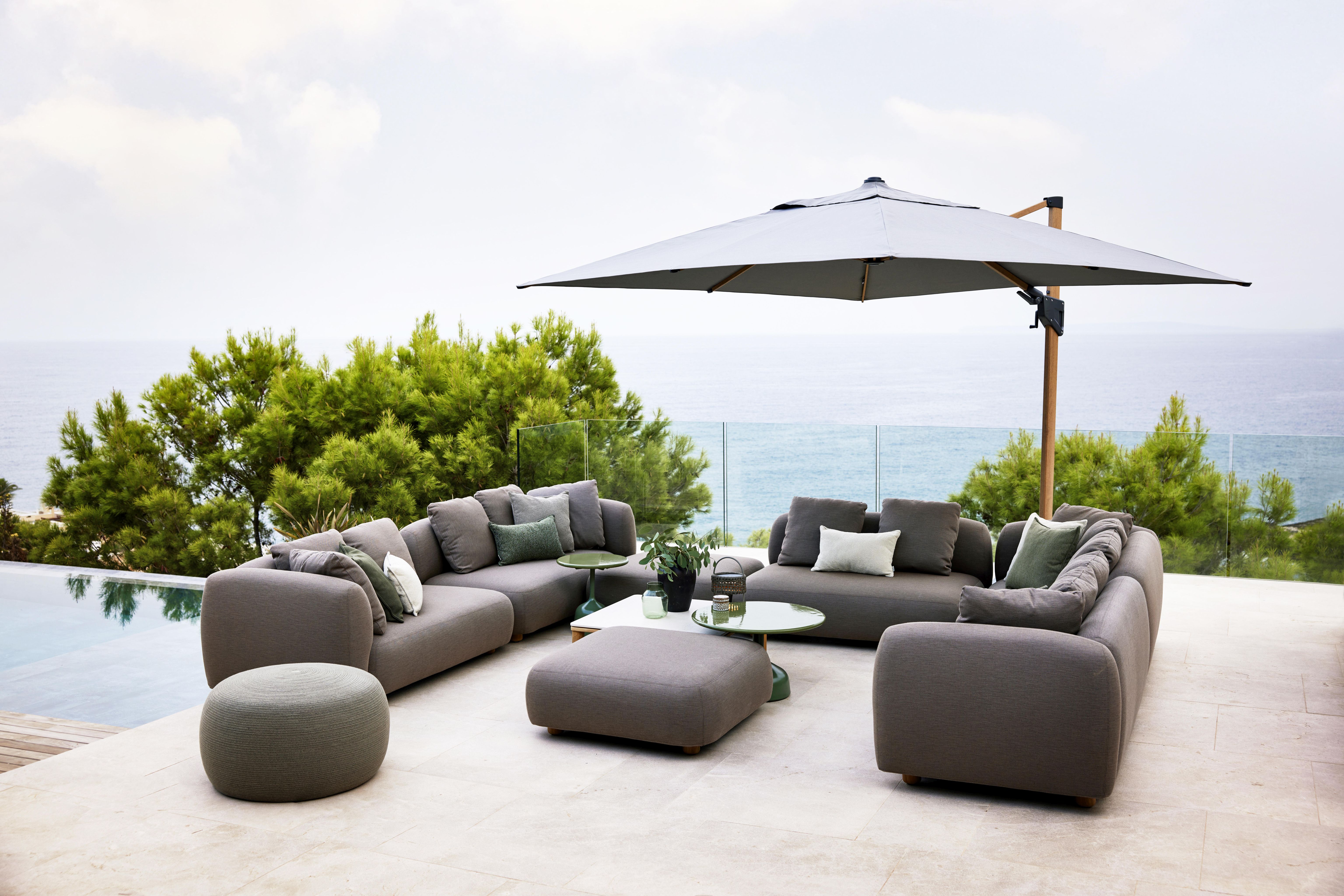 Capture Outdoor Sofa von Cane-Line, graue Lounge-Möbel mit Kissen und Beistelltischen auf einer Terrasse.