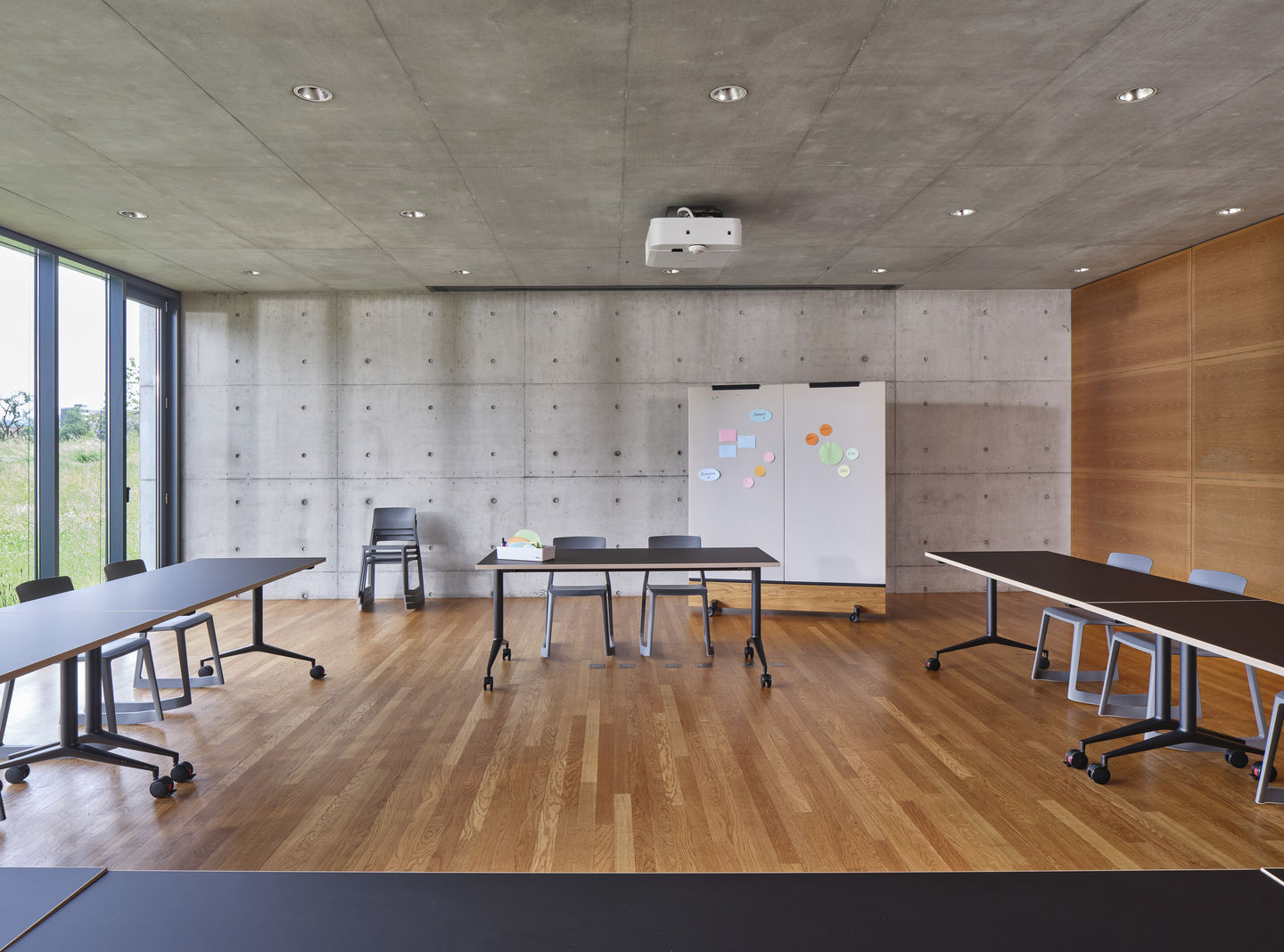 Vitra MedaMorph Klapptische in modernem Konferenzraum mit Betonwand und Holzboden für flexible Arbeitsbereiche.