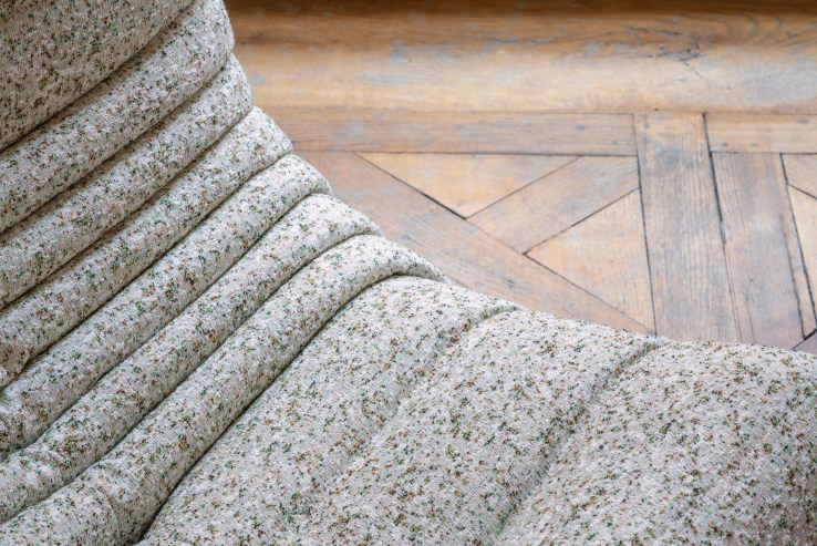 Detailaufnahme des Togo Sessel ligne roset mit beigem Stoffbezug und Falten auf einem Holzboden.