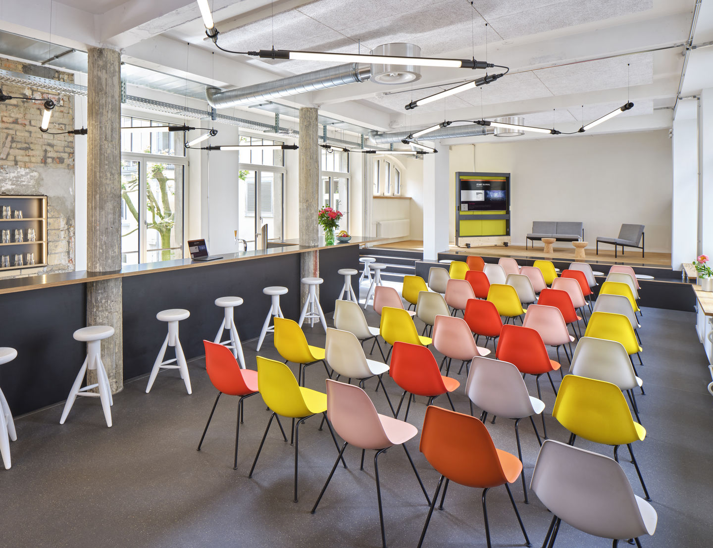 Innenraum mit vielen bunten Eames Stühlen, ideal für Konferenzen oder Veranstaltungen.