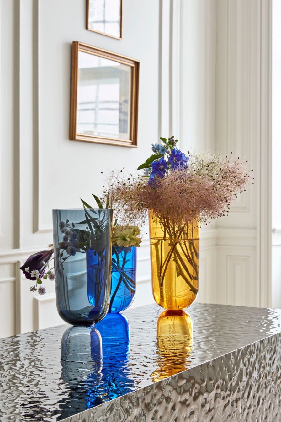 Drei farbige Glasvasen (blau, gelb, türkis) mit Blumen auf einem silbernen Tisch. Dekorative Vasen für Zuhause.
