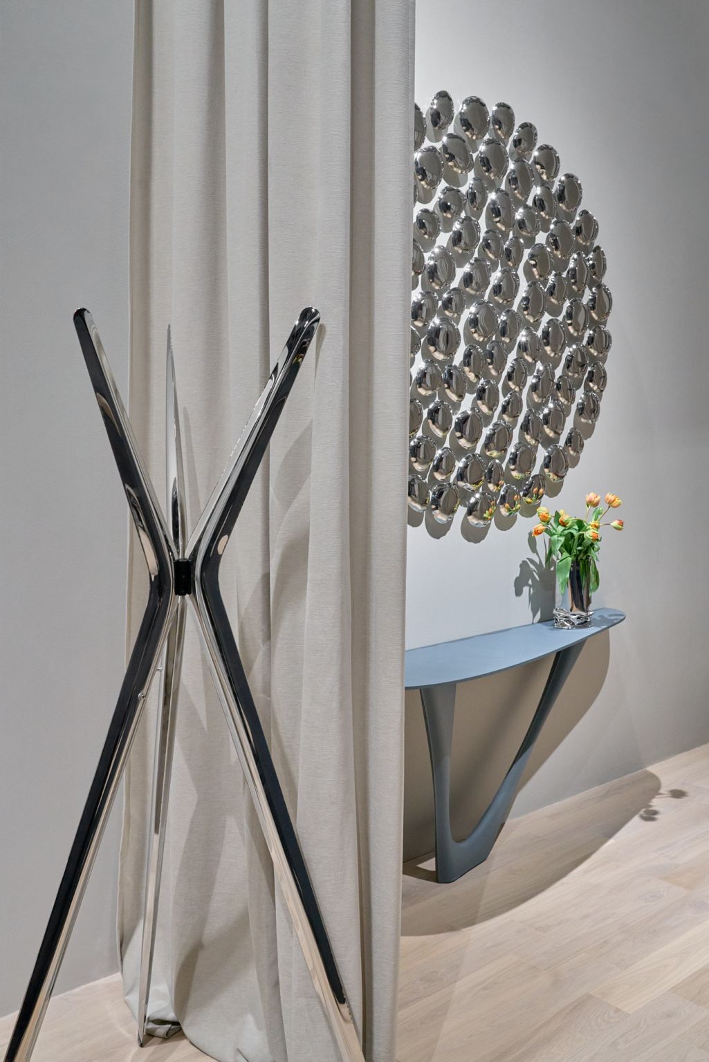 Moderner Kleiderständer aus Chromstahl neben Vorhang, Konsole mit Blumen und Spiegelwand. Designermöbel für stilvolle Einrichtung.