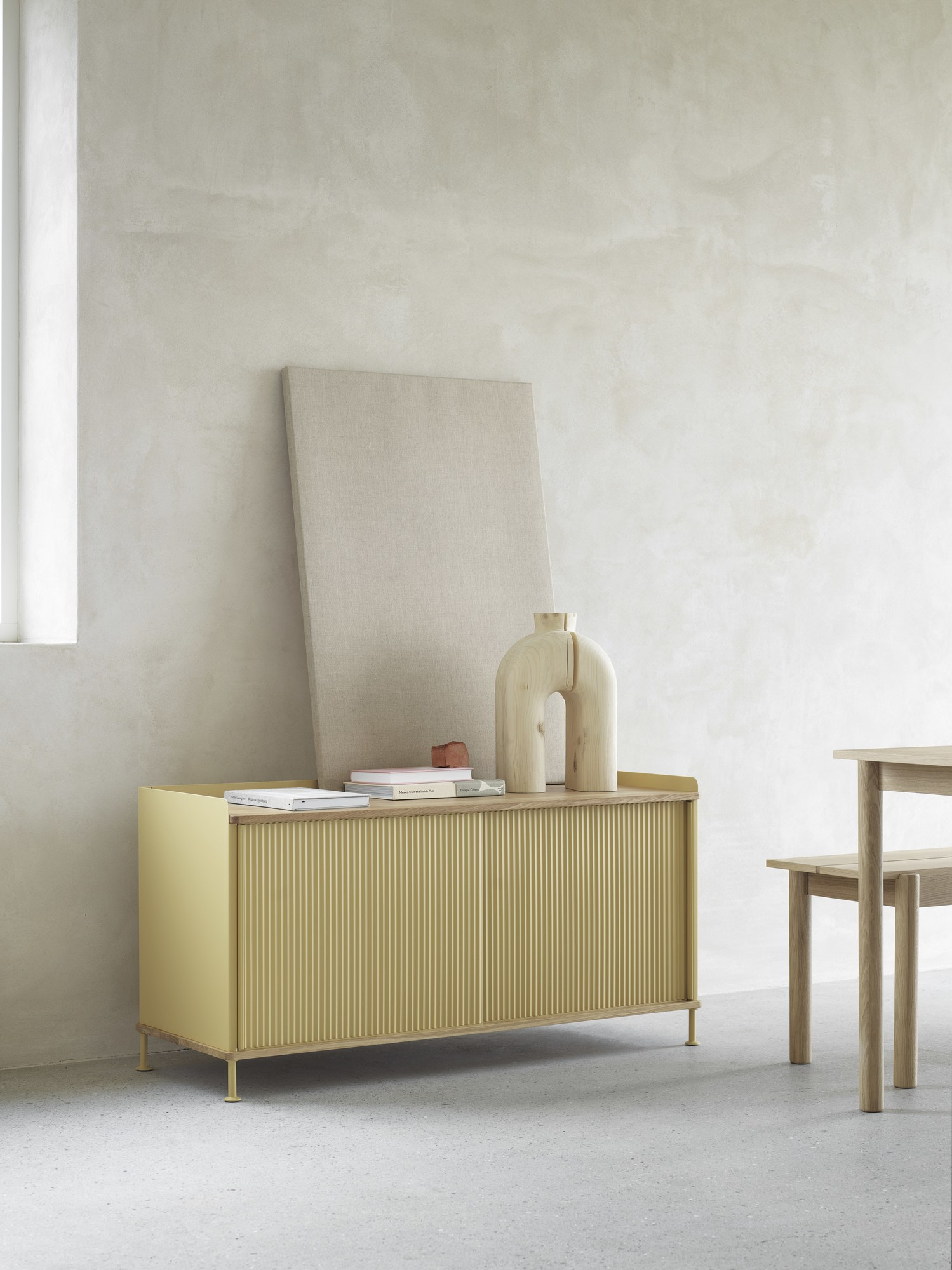 Gelbes Enfold Sideboard Low von Muuto mit geriffelten Türen, Büchern und Holzdeko auf hellem Untergrund.