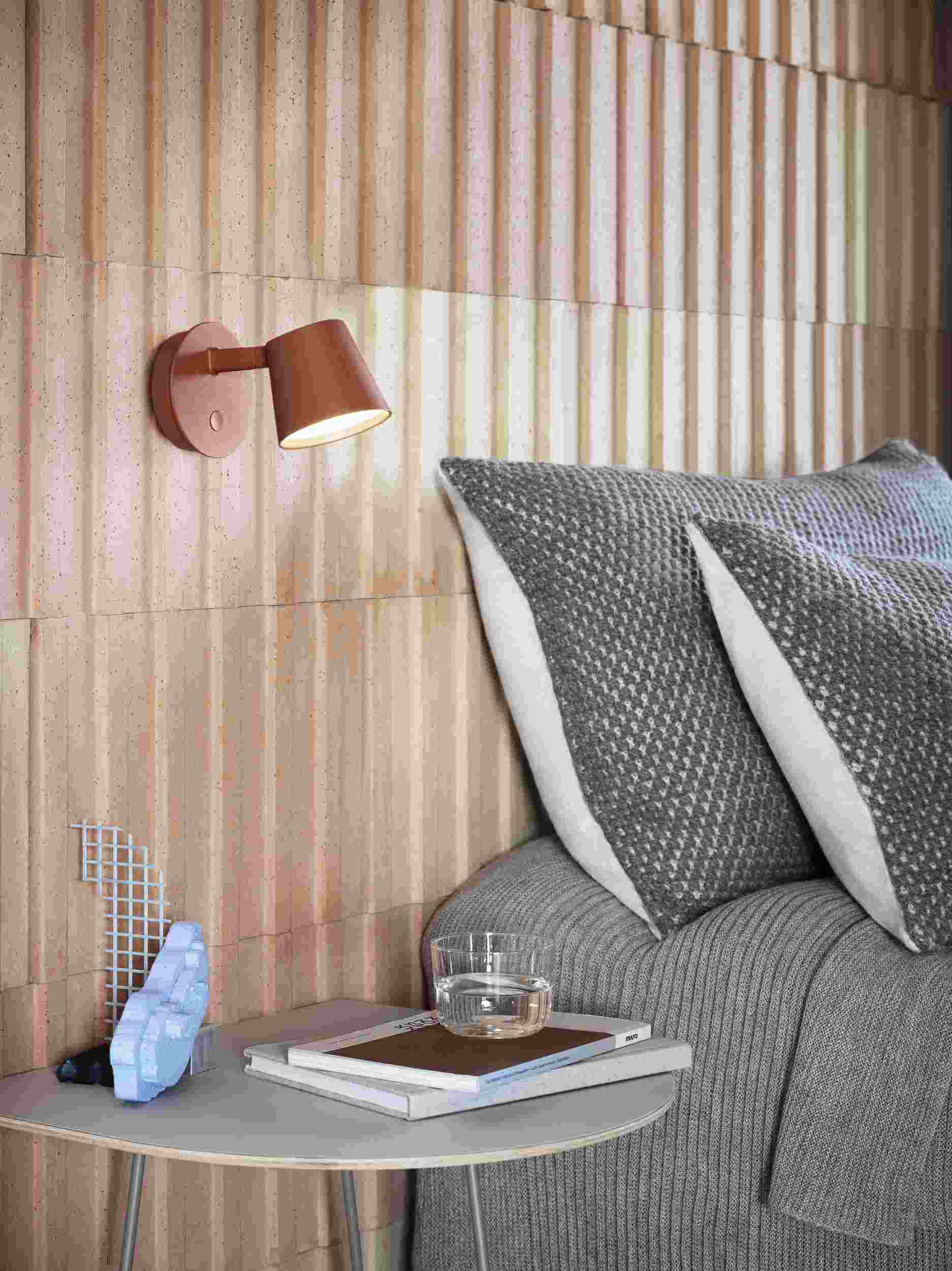 Nahaufnahme der modernen Tip Wandleuchte von Muuto in Weiß, montiert über einem Nachttisch im Schlafzimmer.