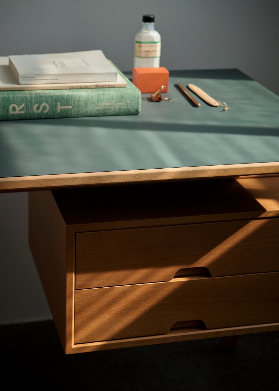 AndTradition Daystak Tisch mit Holzschubladen und grüner Tischplatte, Bücher und Büroartikel im warmen Licht.