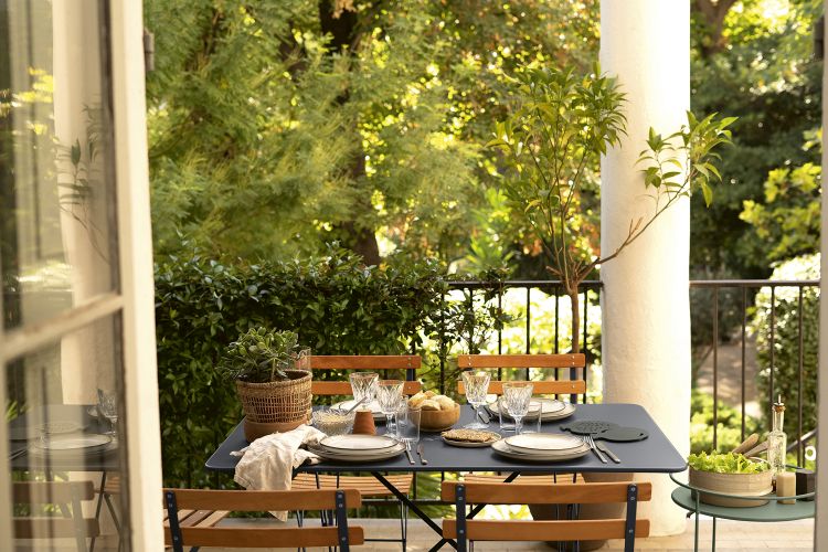 Fermob Bistro Tisch Outdoor auf einem Balkon mit Geschirr und Speisen für ein entspanntes Mittagessen.