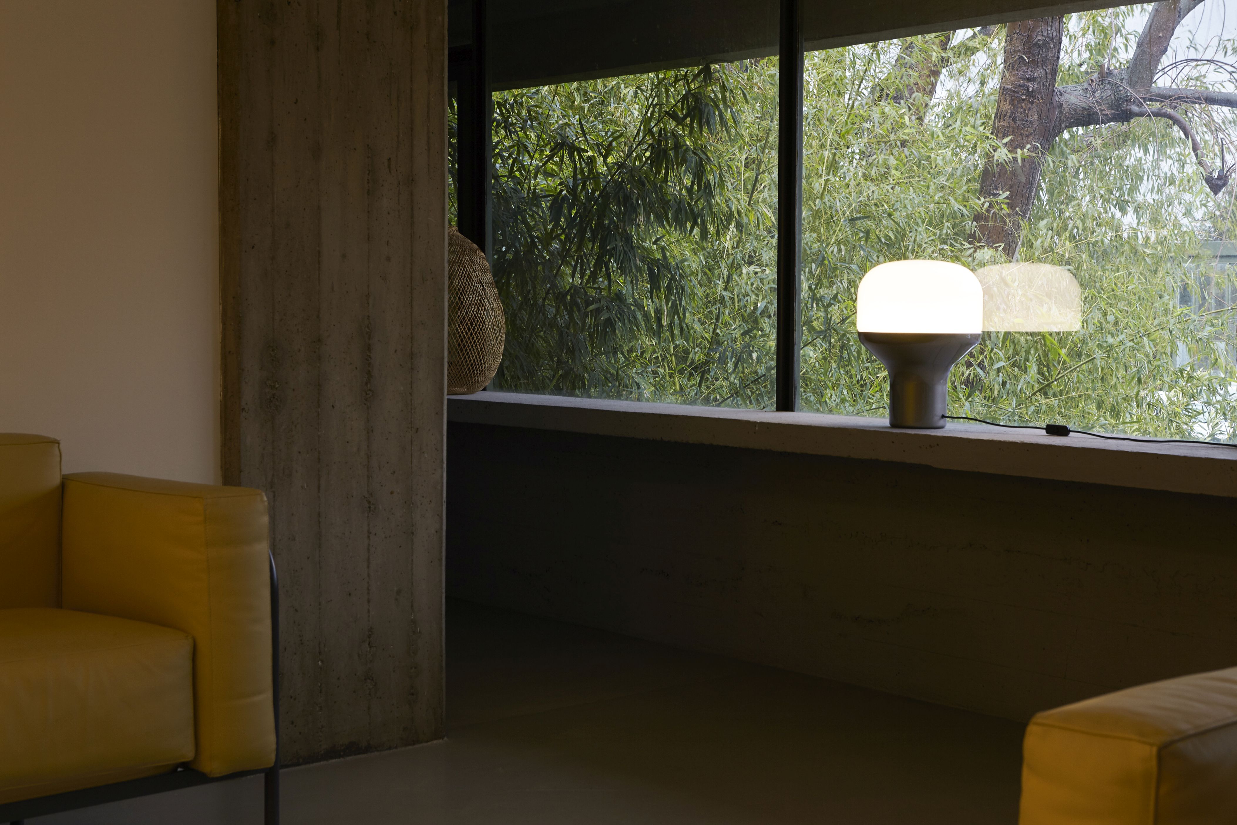 Moderne Martinelli Luce Tischleuchte auf Fensterbank mit Blick auf üppiges Grün, stimmungsvolle Beleuchtung für Wohnzimmer.