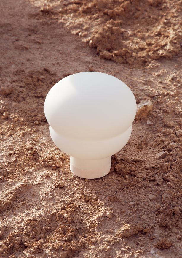 Kumo Tischleuchte von Groß Pulpo, moderne Pilz-Tischlampe aus weißem Glas auf sandigem Untergrund.