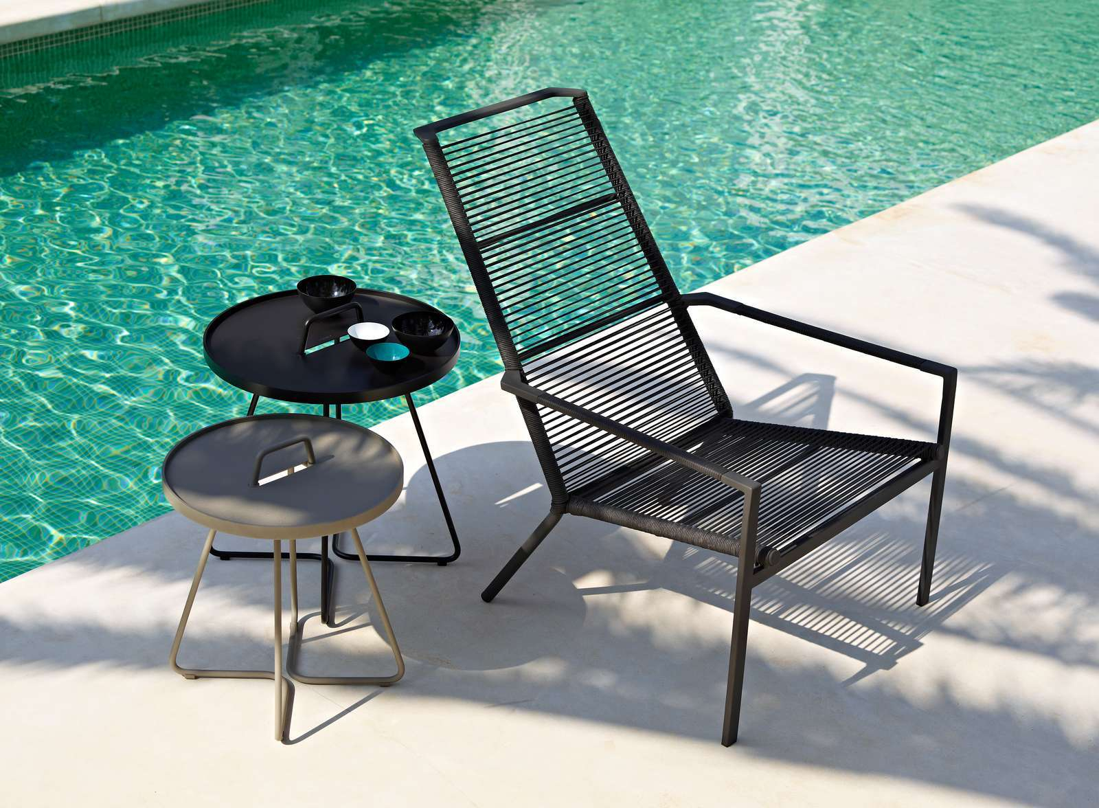 Cane-Line On-The-Move Outdoor Beistelltisch klein in Taupe und ein schwarzer Outdoor Tisch am Pool.