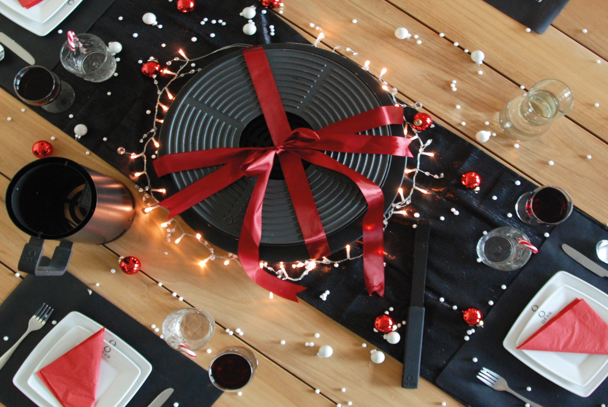 Tabl'O Tischgrill von Ofyr als festliches Geschenk mit roter Schleife und weihnachtlicher Dekoration auf gedecktem Tisch.